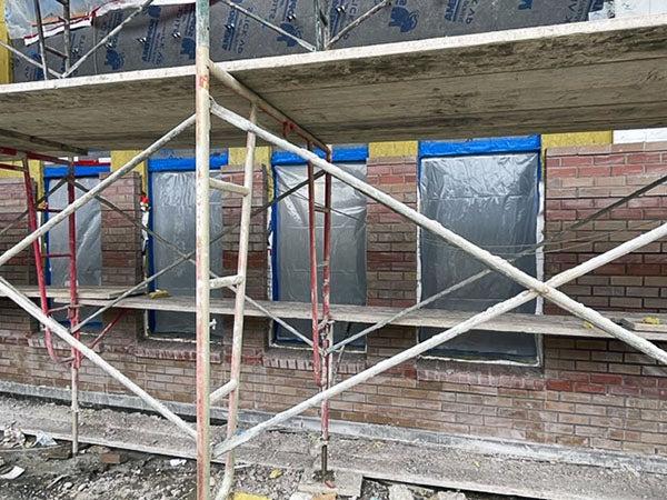 a scaffolding in front of windows with brick partially around them