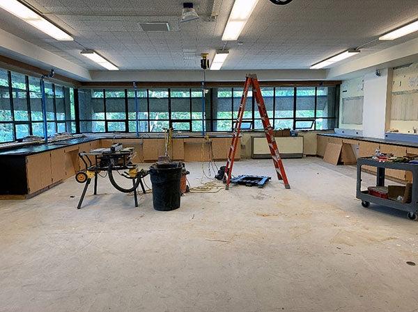 a large room with windows has cabinets partially installed, a ladder, and a table saw